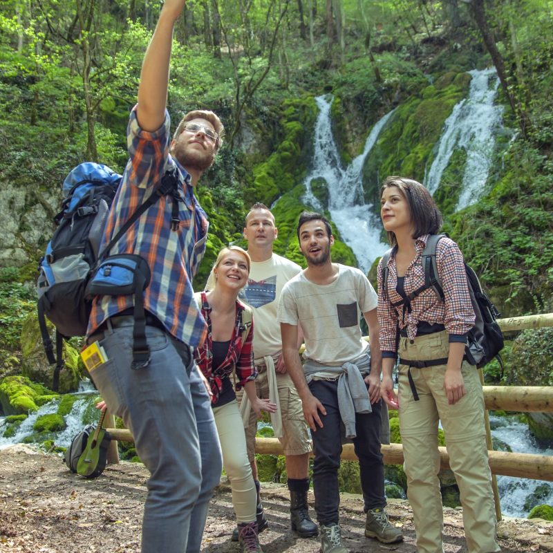 A group of friends having fun and taking selfies in front of a waterfall